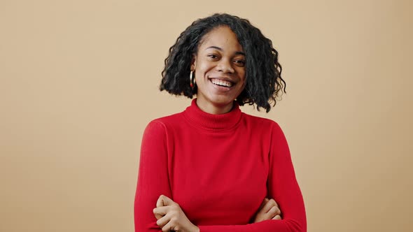 Young Confident African American Woman Laughing to Camera Posing with Folded Arms Over Beige Studio