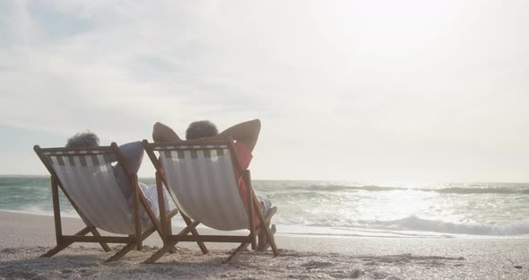 Back view of senior couple relaxing on deckchairs on beach at sunset