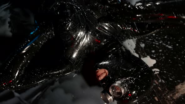 a Woman in a Black Latex Suit and Glasses is Lying on the Dark Floor in a Puddle of White Liquid and