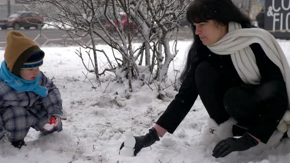 Young Beautiful Mother And Cute Child Play Outdoors During Snowfall. Winter City 8