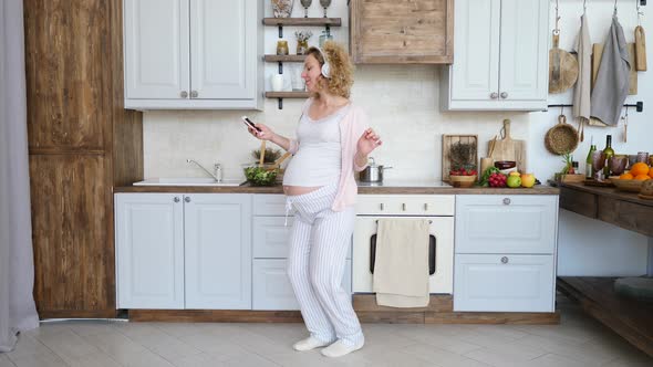 Beautiful Pregnant Girl Dancing With Smartphone On Kitchen