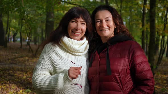 Front View of Two Happy Mature Women with Toothy Smile Looking at Camera Standing in Sunny Park