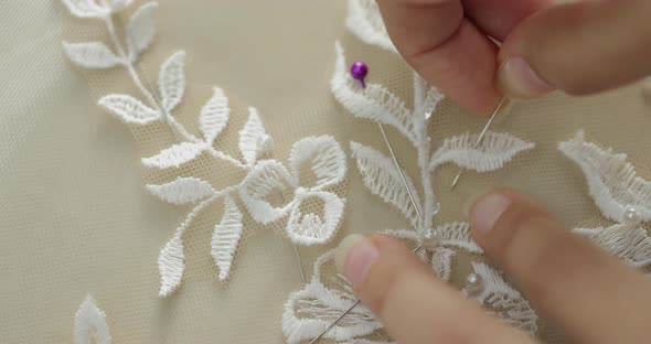 female hands of a seamstress stick a pin into an ivory fabric with a pattern of tree leaves