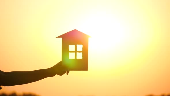 Woman's Hand Holding the House Against a Beautiful Sunset. Silhouette of a House at Sunset