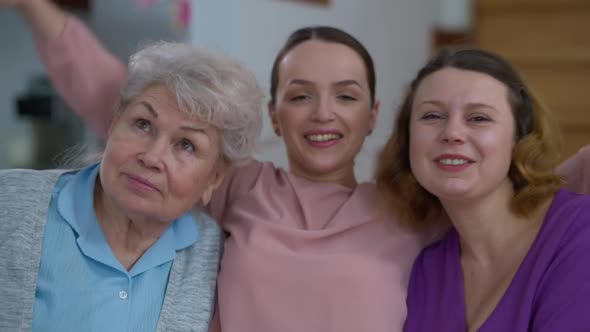 Portrait of Smiling Happy Millennial Woman Hugging Mother and Grandmother Looking at Camera