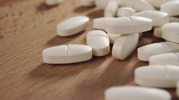 Heap of white oval pharmaceutical medical pills on a wooden surface