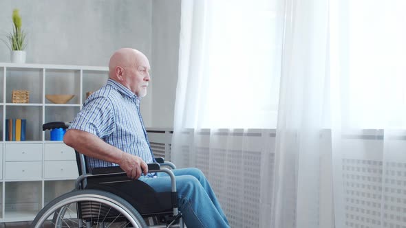 Disabled old man is sitting in a wheelchair at home alone. A handicapped person.