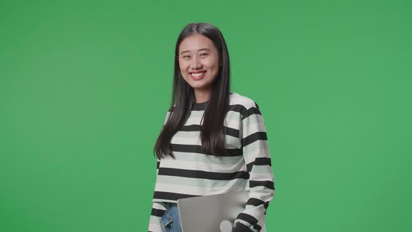 A Smiling Asian Woman Holding Computer While Standing In Front Of Green Screen Background