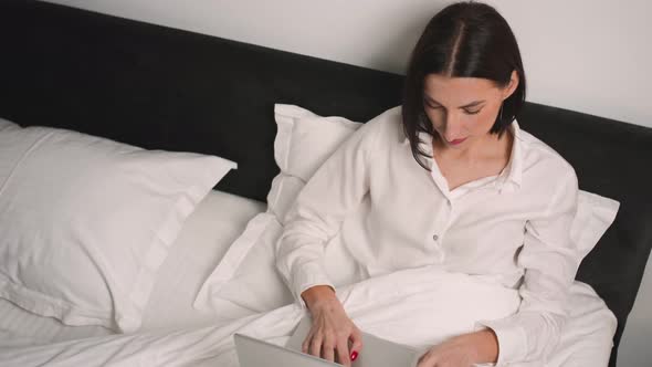 Pretty Caucasian Woman Working Laptop on Bed at Home