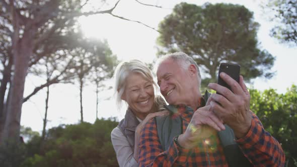 Happy senior couple holding smartphone in forest