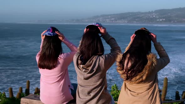 group of three women looking at the sea, putting on colorful caps from pichilemu, punta de lobos