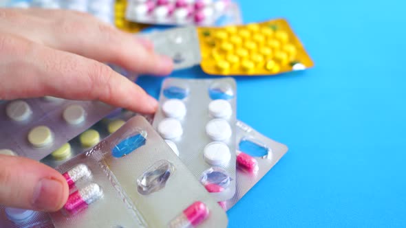 Close Up of Medical Blister Packs with Various Tablets on Blue Background. Man's Hand Selecting