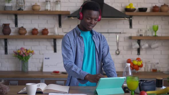 Young Handsome Man with Toothy Smile Surfing Internet on Tablet Standing in Kitchen Indoors