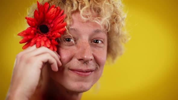 Closeup of Shy LGBT Man with Red Flower in Hair Posing at Yellow Background