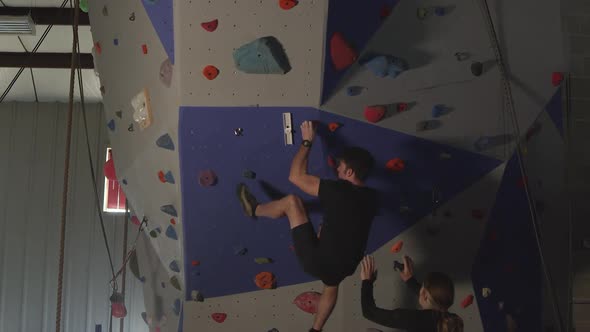 Couple in gym working out on rock climbing wall