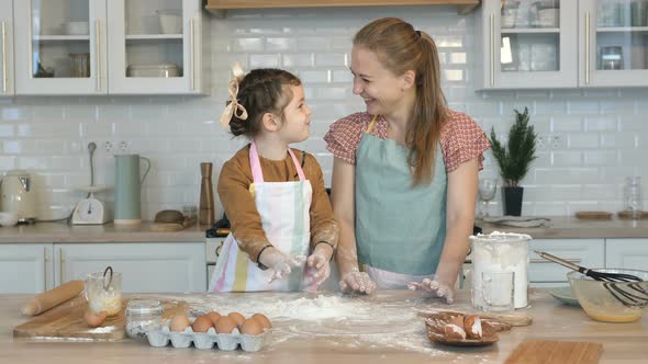 Happy Mother and Daughter Cook Together in the Kitchen, Throw Flour on the Table and Laugh. Have Fun