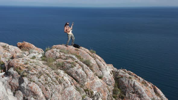 Man Playing Acoustic Guitar in Nature in the High Rock Near Sea