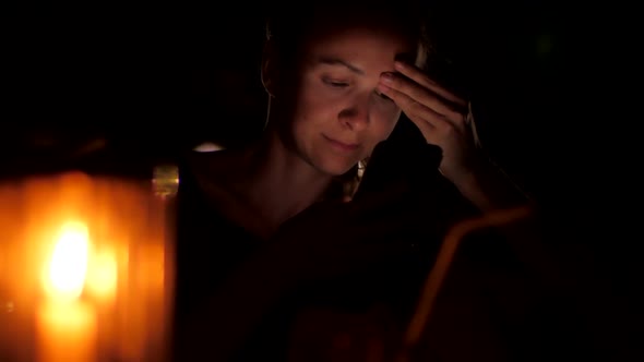 Lady Sits at Night Behind Candle Holding Black Smartphone