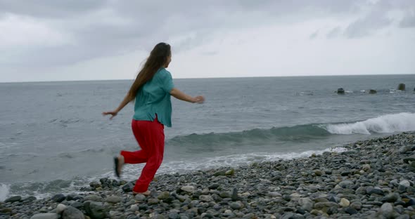 Pretty Lady Runs Along Grey Pebble Beach Under Cloudy Sky