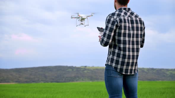 Close Up of Man Farmer in Hat Standing in Green Wheat Field and Controlling a Drone Which Flying