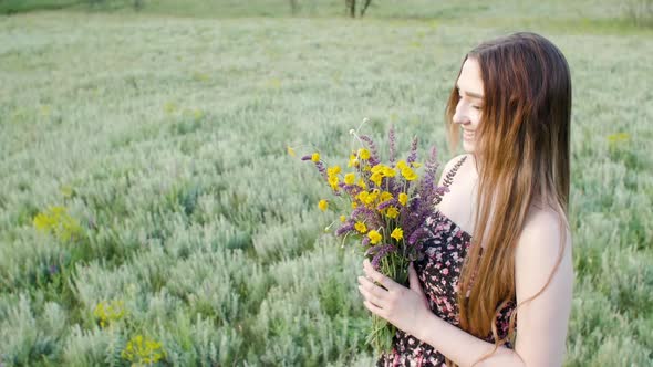 beautiful girl with bouquet of wildflowers on meadow, young woman with long hair in dress 
