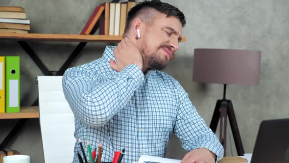 Tired student writes in notebook massaging neck after over work at laptop