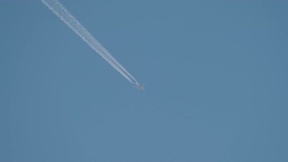 Distant Passenger Jet Plane Flying on High Altitude on Clear Blue Sky Leaving White Smoke Trace of