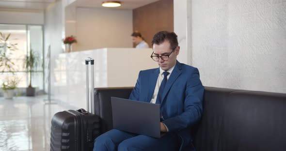 Young Businessman Using Laptop Sitting in Modern Hotel Lobby