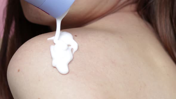 white cream,body lotion pouring from the tube on woman naked shoulder or on the hand.girl is applyin