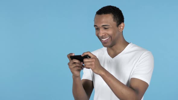 Young African Man Playing Game on Smartphone Blue Background