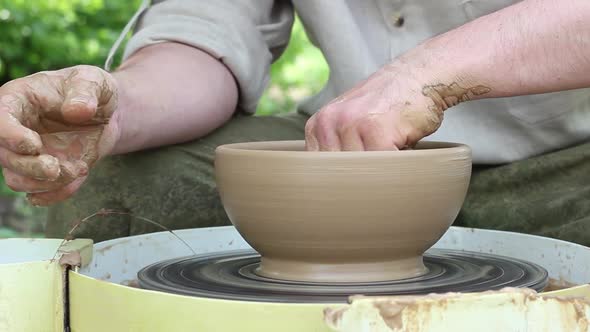 Caucasian Male Potter Removes Moisture with Yellow Sponge From an Earthen Pot on an Electronic