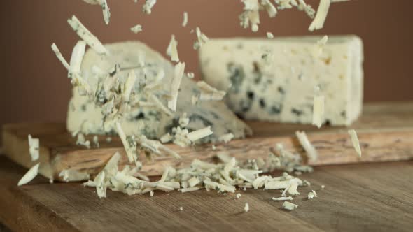 Super Slow Motion Shot of Grated Blue Cheese Falling on Wooden Board 