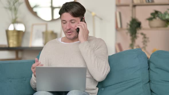 Middle Aged Man with Laptop Talking on Smartphone, at Home
