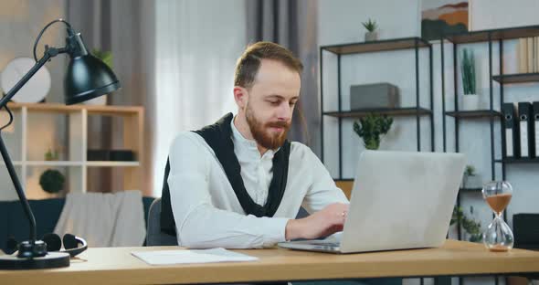 Bearded Man Sitting at the Table at Home and Working on computer