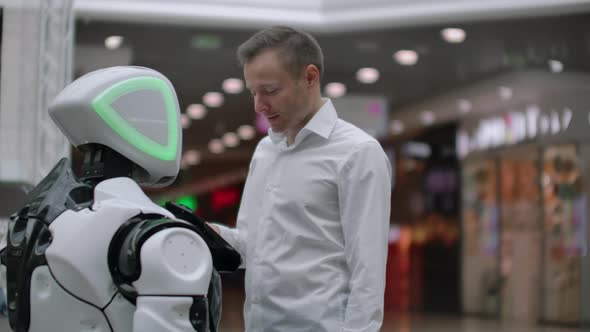 A Man Stands with a Robot Bot and Asks Him Questions and Asks for Help By Clicking on the Screen on