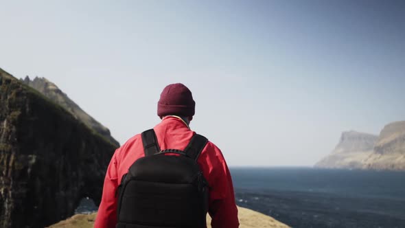Male Traveler with Backpack Walking Slowly on Edge of the Cliff in Drangarnir