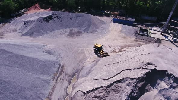 A bulldozer is gaining rubble. The territory of the granite quarry, top view from the copter.