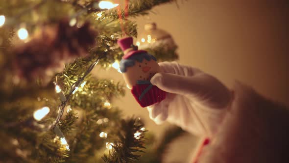 Santa Claus reaching to look at a snowman ornament.
