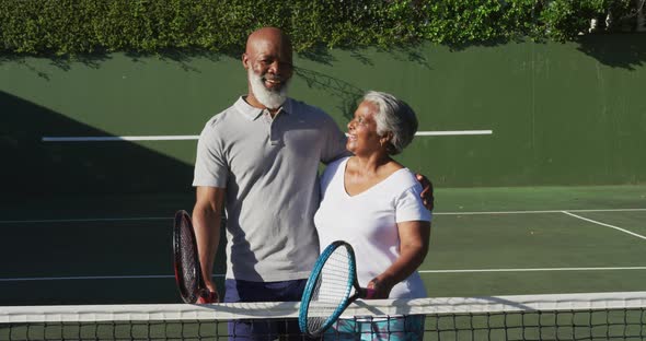 Portrait of african american senior couple holding rackets standing on the tennis court