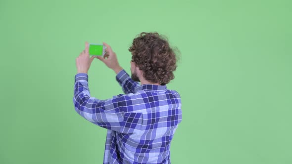 Rear View of Young Bearded Hipster Man Taking Picture with Phone