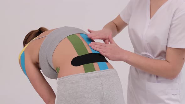 Demonstration video of a therapist taping kinesio tape on a female patients back