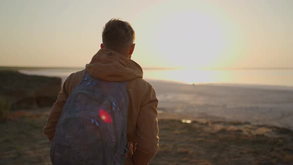 Camera Follows Man Traveler with Backpack Meeting Sunrise at Deserted Sea Beach