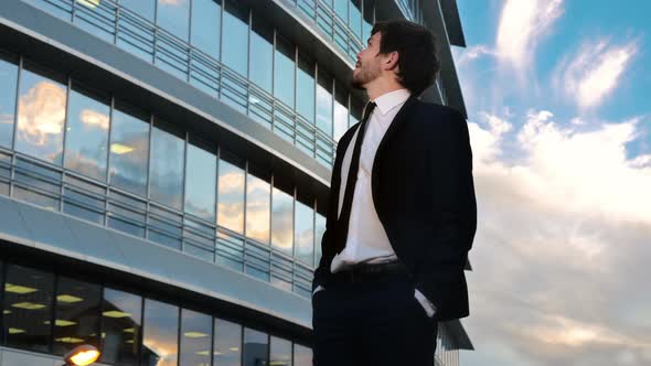 Young Businesssman Looking Up with Smile Day Dreaming Standing in Front of Business Center