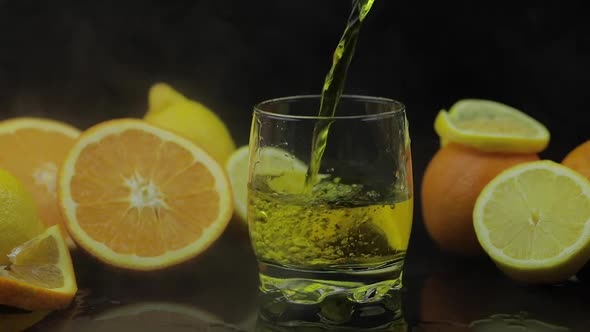 Pour Juice Into Glass, Orange and Lemon Slices on Background. Slow Motion