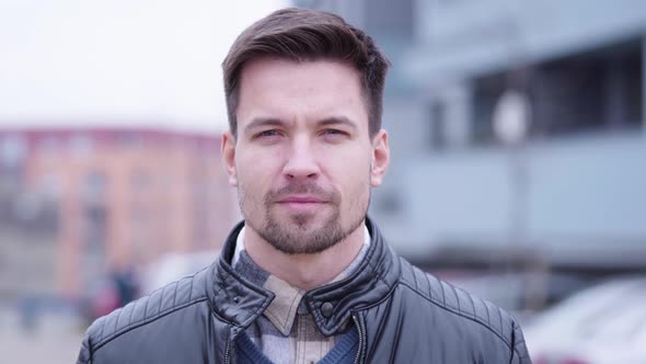 A Young Handsome Man Smiles at the Camera in a Suburban Area with Buildings in the Blurry Background