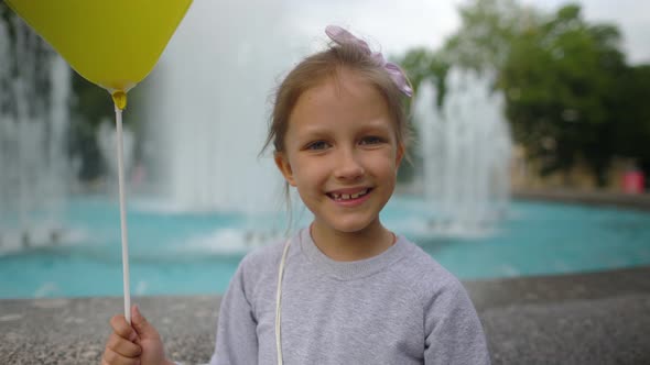 Girl With Yellow Balloon Near Fountain In City