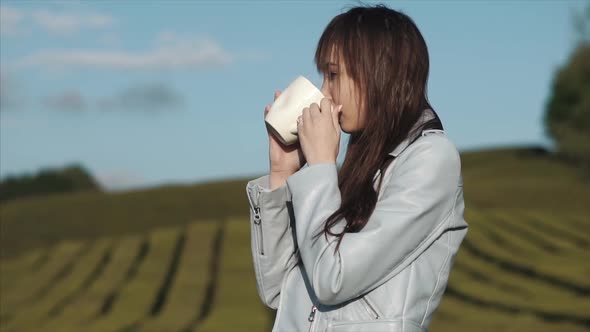 Charming Woman Is Drinking Tea From Big White Cup Standing on a Tea Plantation