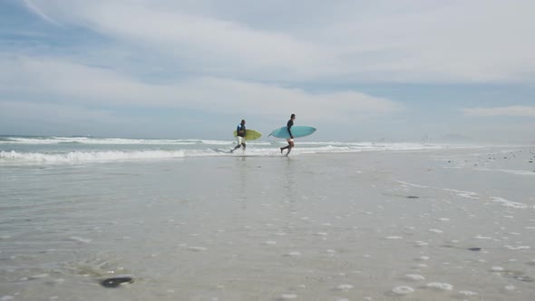 African american father and teenage son walking on a beach holding surfboards and talking