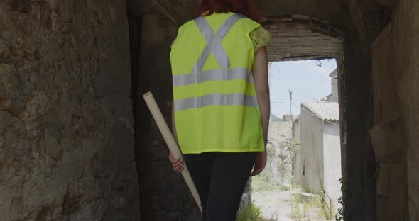 Young female architect or engineer walks down a street between abandoned houses