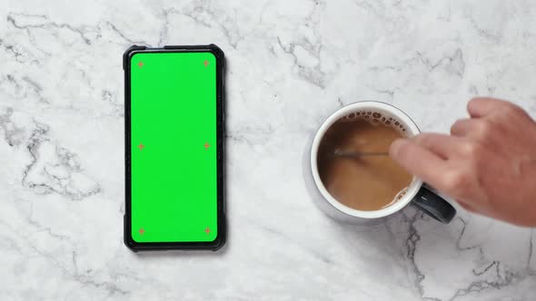Woman hand stirring hot coffee and using smartphone with green screen